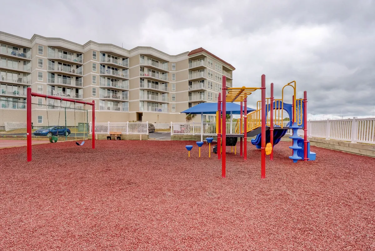 An exterior image of a vibrant playground with swings and colorful equipment, set on rubberized ground near the apartment building. Children and families are seen enjoying the outdoor play area, suggesting a lively, inclusive, and safe environment for all ages.