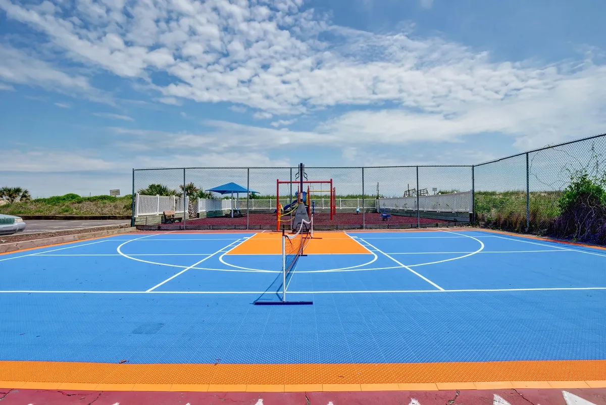 A brightly colored outdoor court with a basketball hoop and netting creates a playful, energetic mood. The expansive play area is designed for games like basketball and tennis, ideal for social gatherings and friendly competition.