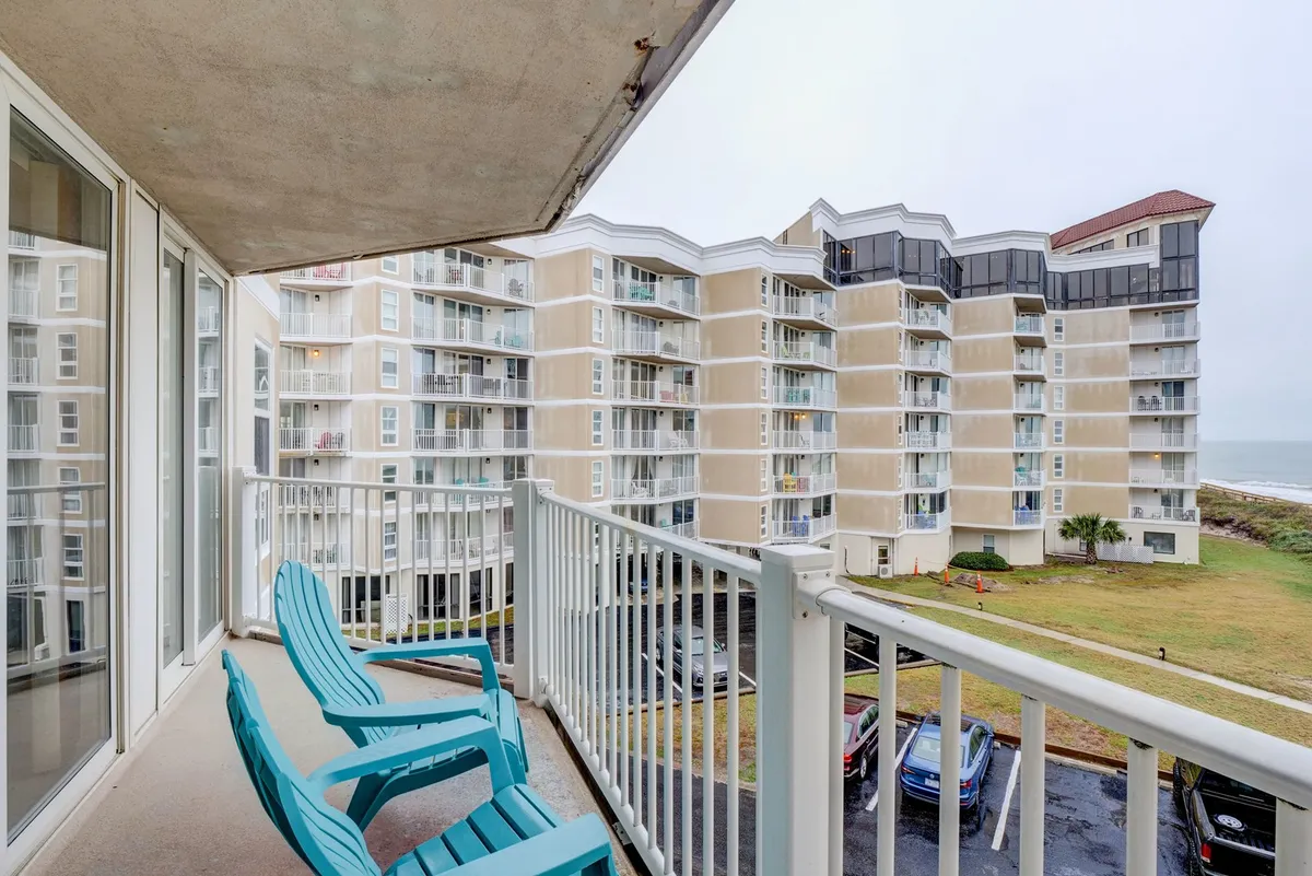 This image showcases a private balcony with comfortable seating, set against a sweeping ocean view. The building's architecture is visible, but the focus is on the tranquil experience of relaxing on the balcony and enjoying the sea breeze.