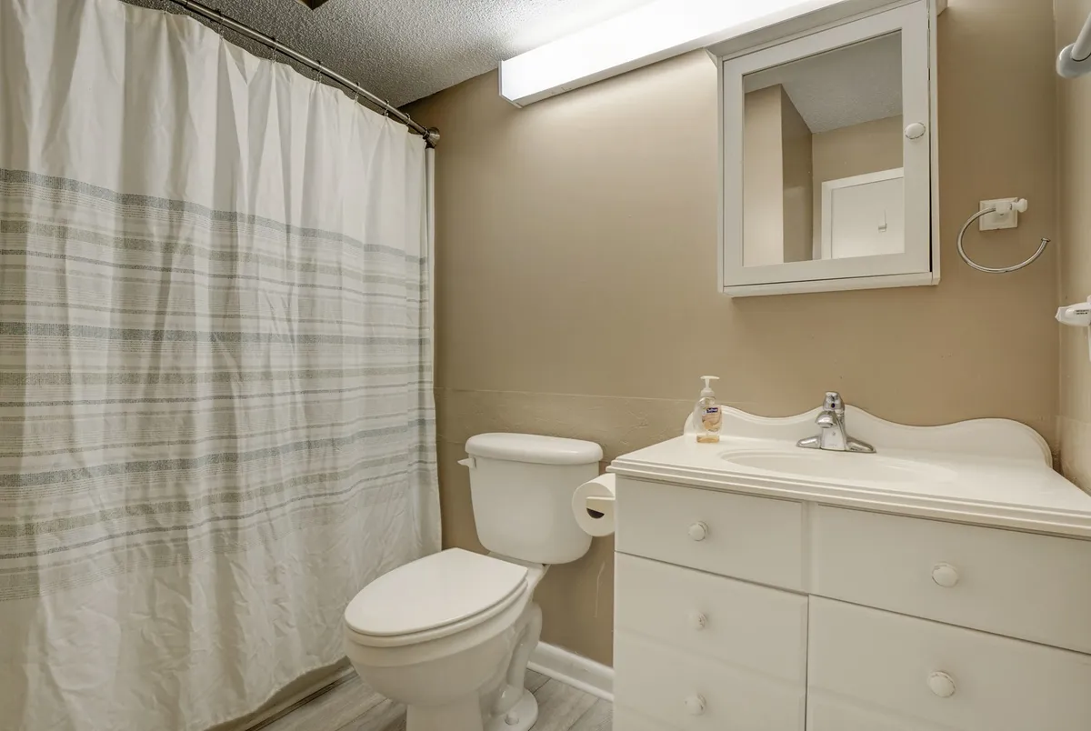 A clean and practical bathroom with a vanity and mirror, a toilet, and a shower curtain. The space is well-lit and organized, providing a private area for self-care and daily routines.