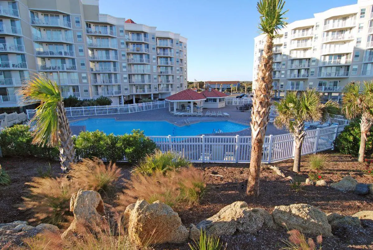 This image captures the outdoor swimming pool surrounded by palm trees, with ample outdoor seating and a paved patio area. The tranquil setting suggests both relaxation and social gatherings, with children potentially playing in the water and families unwinding by the pool.
