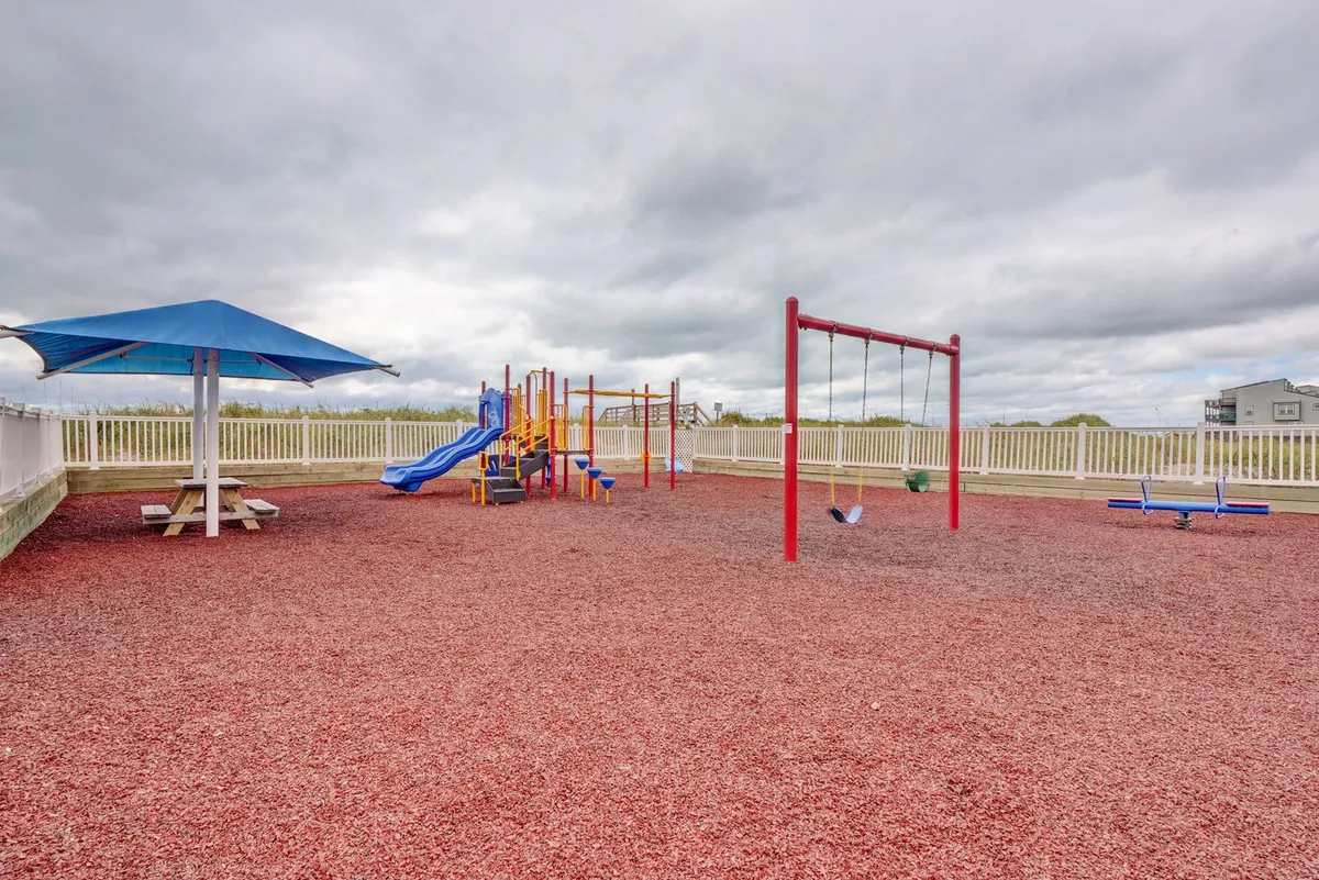 A colorful outdoor playground with swings and a picnic table under an umbrella, set up for children and families to gather and play. The scene is joyful, highlighting laughter and community enjoyment.