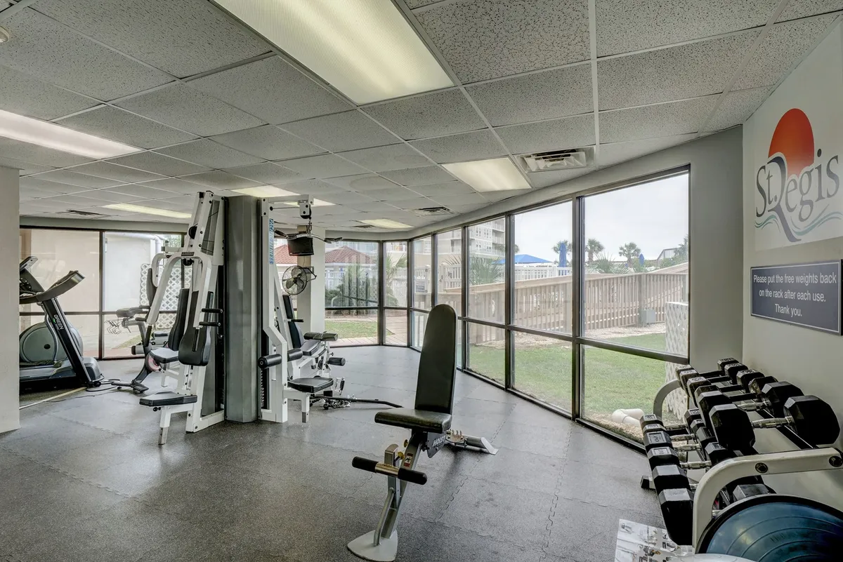 The fitness center is filled with exercise machines, a weight rack, and large windows that let in natural light, offering a glimpse of the outdoors. The bright, energetic atmosphere encourages daily workouts and personal wellness routines.