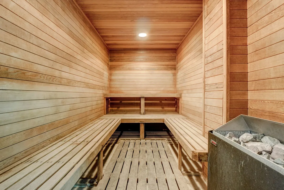 A serene sauna interior with smooth wooden benches and walls, centered around a traditional heater. The space is calm and inviting, perfect for post-workout relaxation or quiet, restorative moments for two.