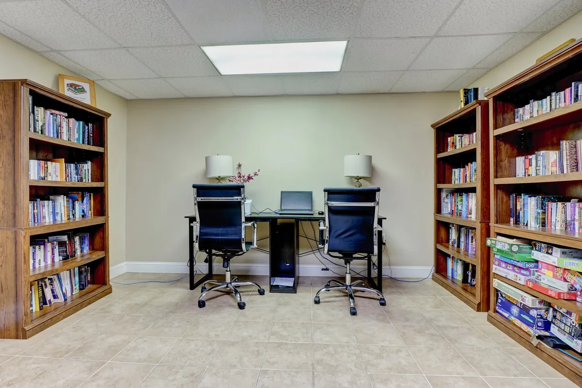 A productive work environment is depicted here, with bookshelves, desks, a computer setup, and ample lighting. The space is designed for reading, working remotely, or quiet contemplation, conveying a sense of focus and comfort.